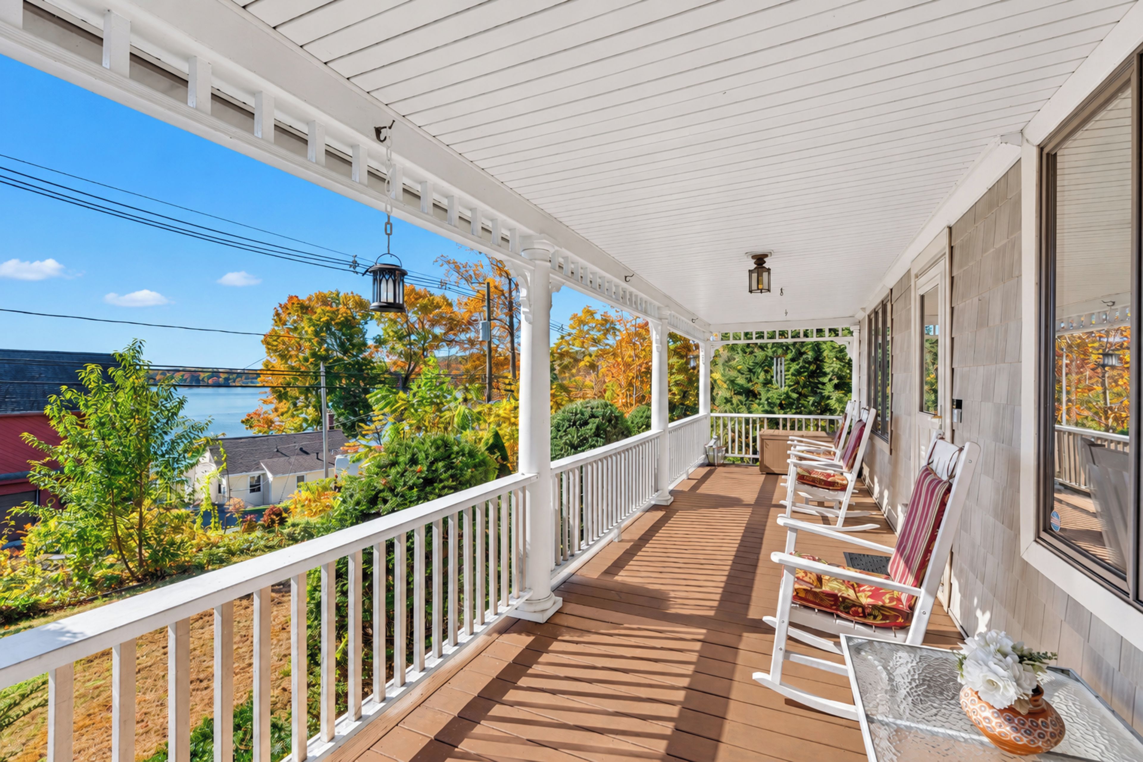 A covered porch with a view of a lake and autumn foliage.