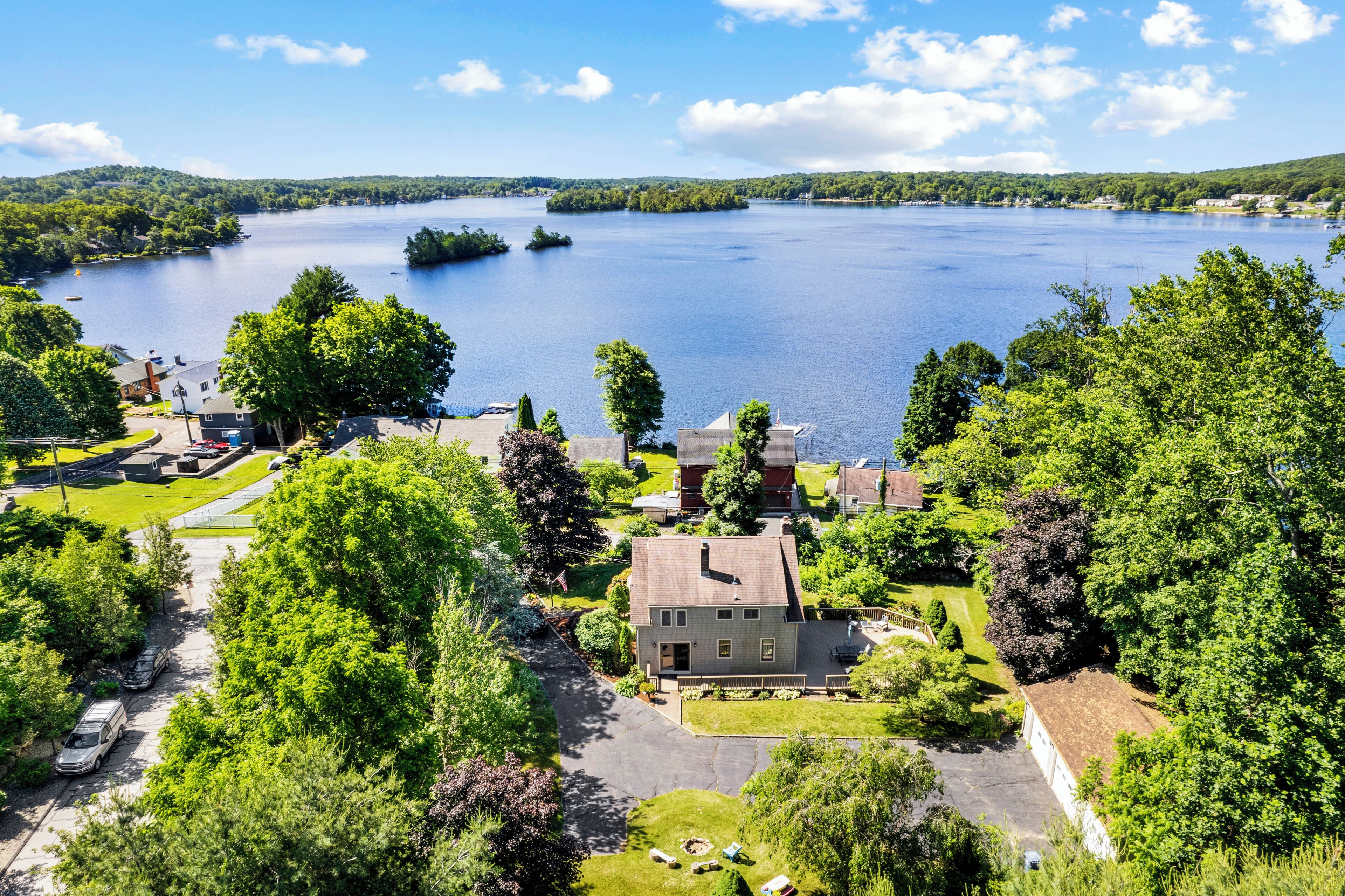 A lakeside property with a house, a driveway, and surrounding greenery.