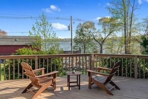 A wooden deck with two Adirondack chairs and a small table, overlooking a body of water and trees.