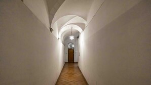 Un estrecho pasillo con paredes blancas y suelo de madera, que conduce a una puerta con un vitral.