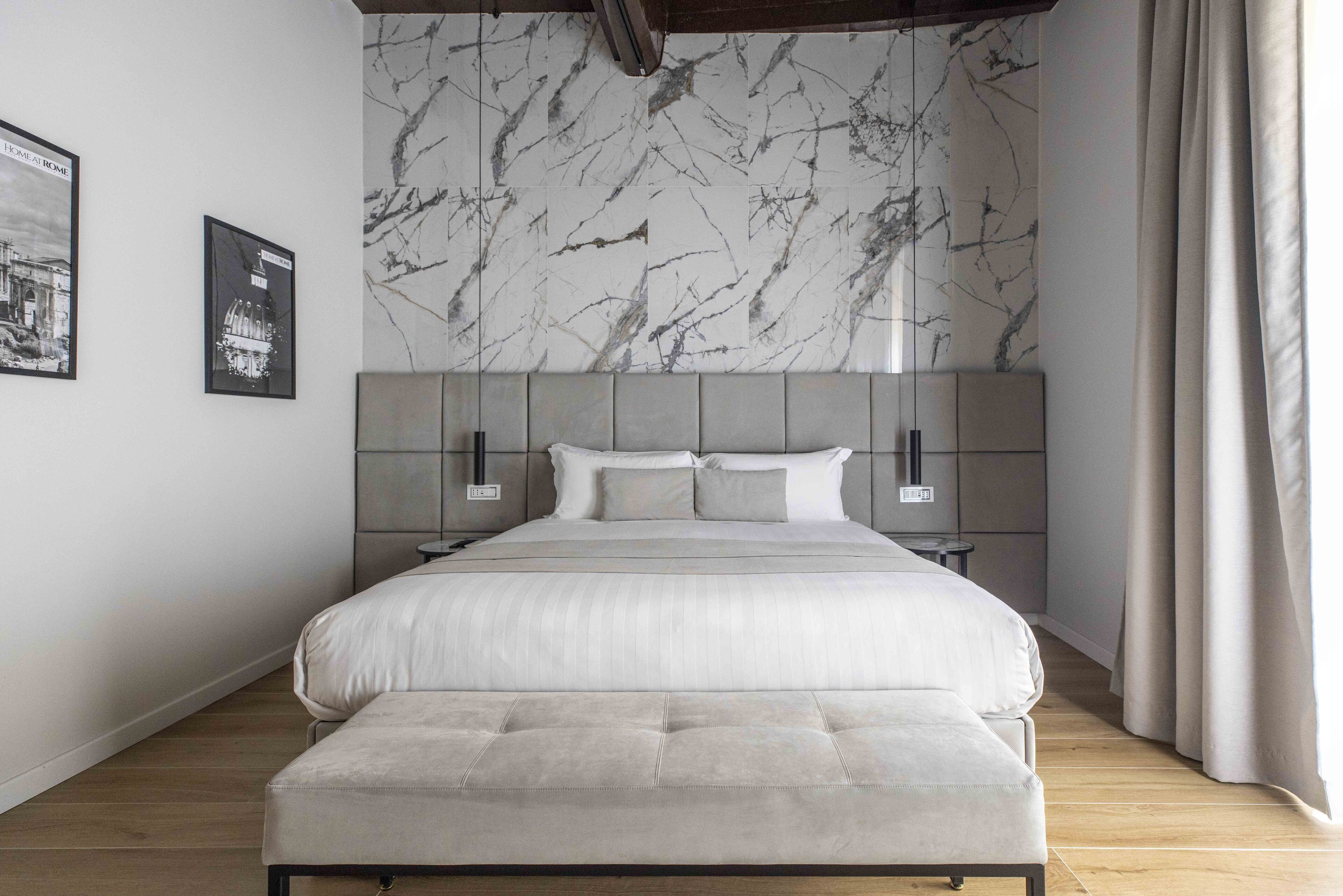 A modern bedroom with a marble-patterned headboard, a large bed with a tufted bench, and two bedside tables.