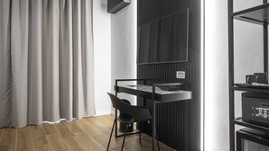 Una habitación moderna con suelo de madera, un escritorio con silla, una estantería negra y un amplio ventanal con cortinas.