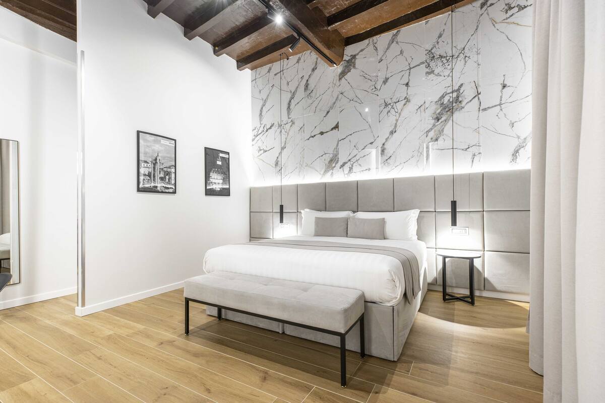 A modern bedroom with a large bed, a bench, a nightstand, and a marble wall.