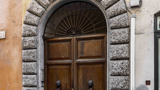 Puerta doble de madera con arco de piedra, un tirador de metal y una placa con el número 101.