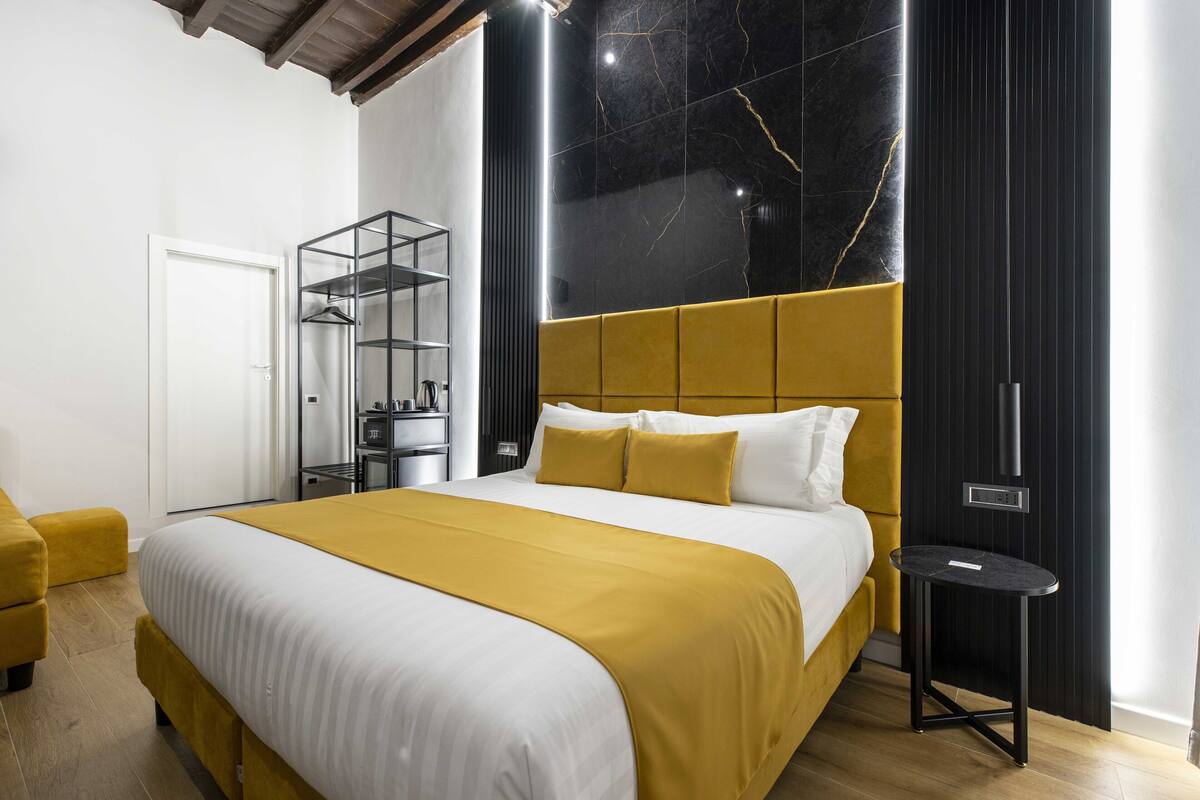 A modern bedroom with a large bed, a bedside table, a wardrobe, and a mirror.