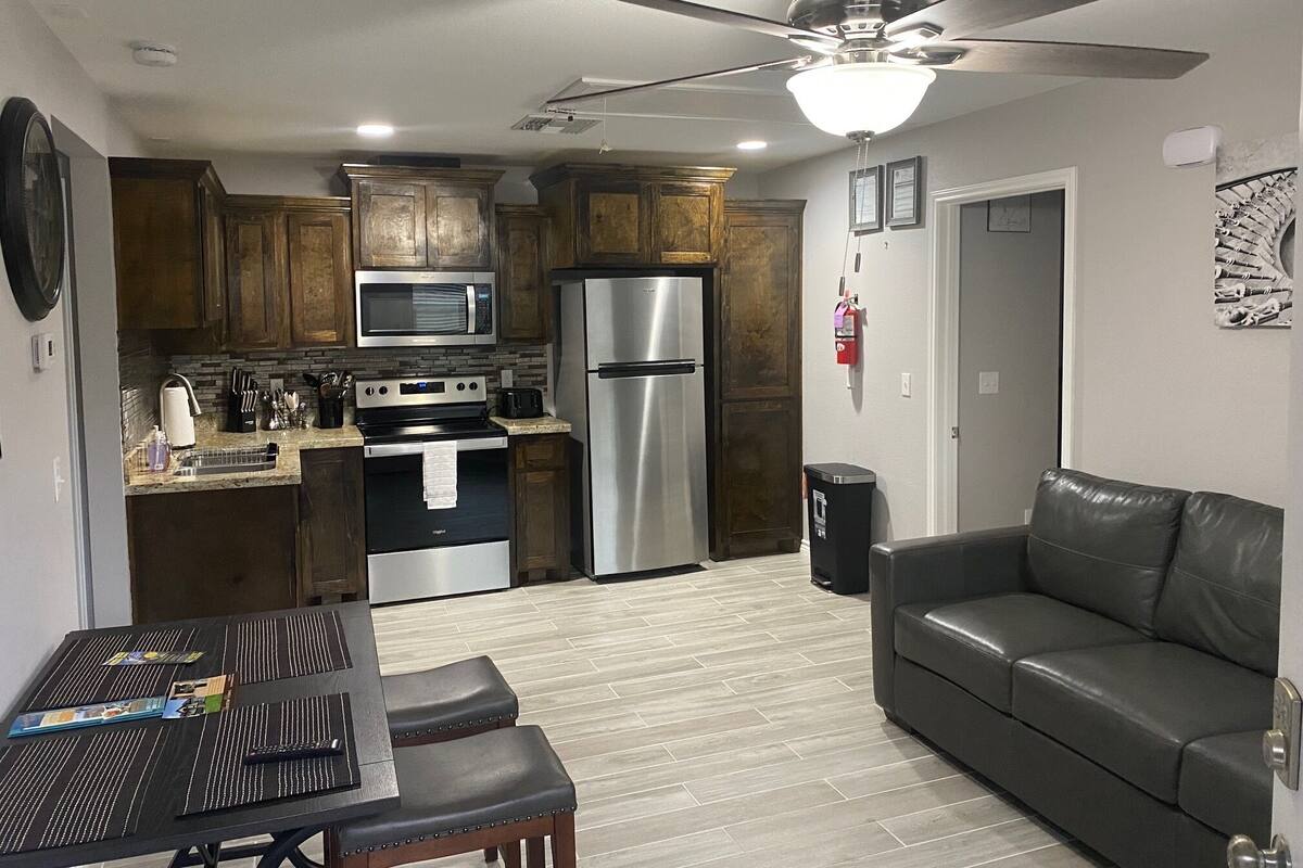A compact kitchen with a microwave, stove, and refrigerator. There is a dining table with chairs and a leather sofa.
