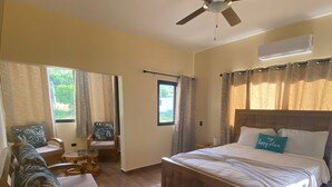 A hotel room with a bed, a ceiling fan, an air conditioner, a window with curtains, a sofa, and a small table. - Romantic VillaLunaCaridad (Jarabacoa)