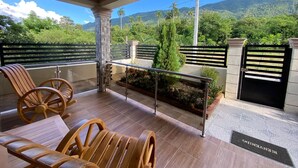 A balcony with wooden chairs and a glass table, overlooking a lush green landscape with mountains. - Romantic VillaLunaCaridad (Jarabacoa)