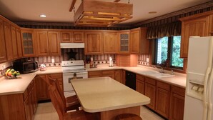 A kitchen with wooden cabinets, a central island, a microwave, stove, and a refrigerator. - Whitetail Ridge Cabin ,Sleeps 10 (Loudonville)