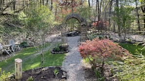 A garden with a gravel path leading to a wooden archway, surrounded by trees and shrubs. - Whitetail Ridge Cabin ,Sleeps 10 (Loudonville)
