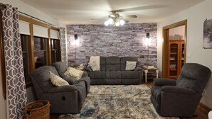 A living room with a stone wall, two sofas, a ceiling fan, and a wooden floor. - Whitetail Ridge Cabin ,Sleeps 10 (Loudonville)
