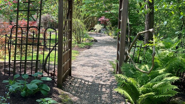 A garden pathway leading through a wooden archway, surrounded by lush greenery and flowering plants. - Whitetail Ridge Cabin ,Sleeps 10 (Loudonville)
