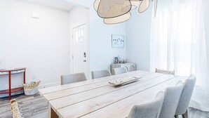 Uma sala de jantar com uma mesa de madeira, cadeiras estofadas cinzas, um cesto trançado e um lustre.
