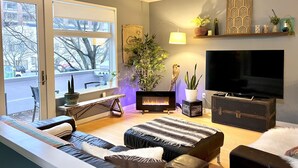 Ein modernes Wohnzimmer mit Kamin, großem Fernseher und einem Balkon mit Blick auf die Stadt.
