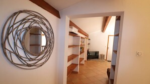 A hallway with a woven wall decoration, wooden shelves, and a tiled floor. - Villa Port Camargue – Private pool, air conditioning, free parking (LE GRAU DU ROI)
