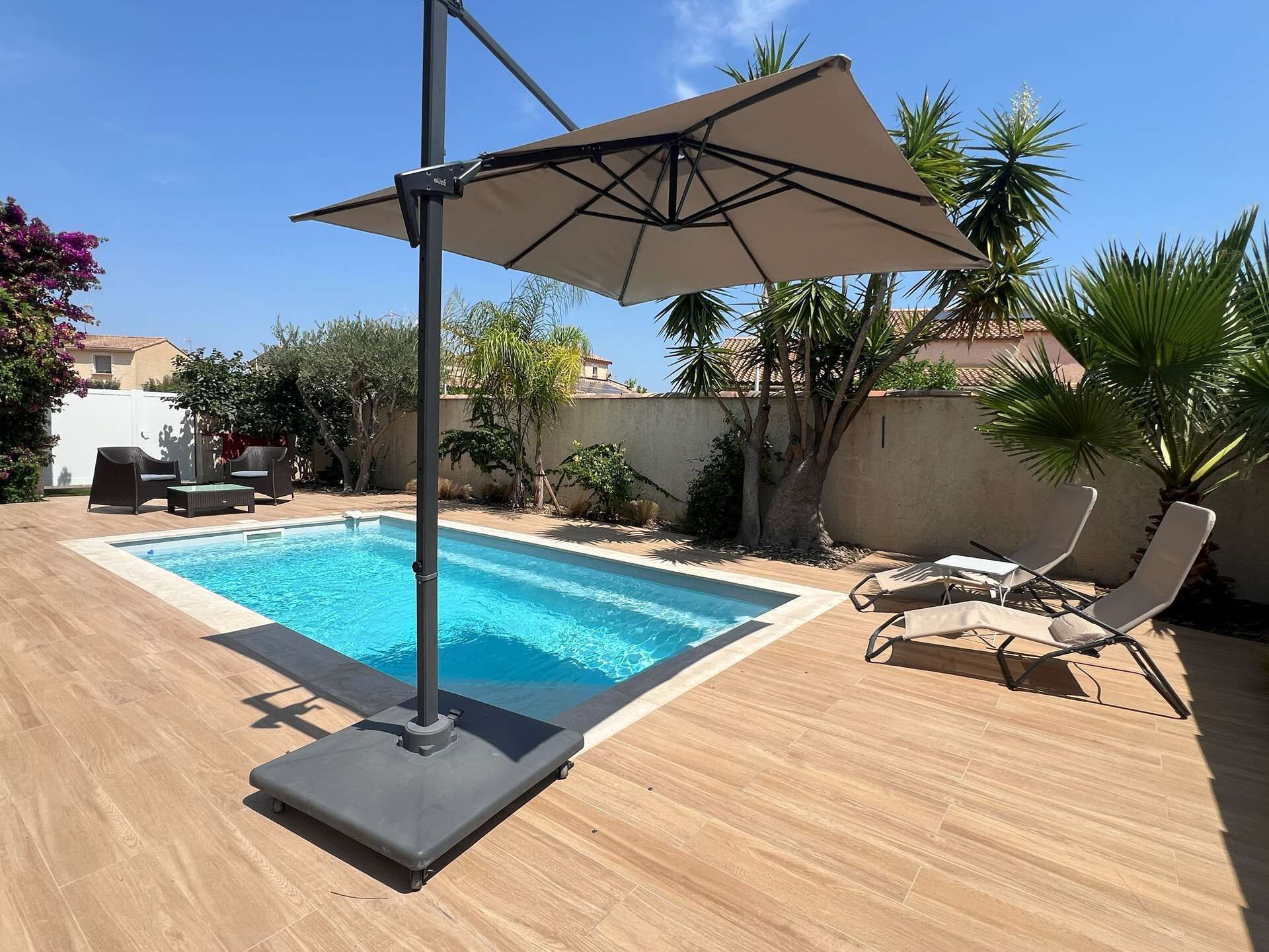 A swimming pool with a sun umbrella, lounge chairs, and a wooden deck.