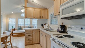 Cocina compacta con armarios de madera, estufa blanca y una zona de comedor con una mesa y sillas.