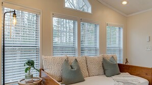 Un dormitorio con cama de madera, ropa de cama blanca y varias ventanas con persianas.
