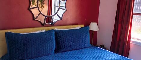 Un lit avec une couette bleue, un miroir décoratif et un ventilateur de plafond.