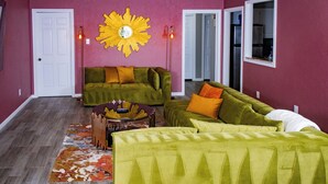 Uma sala de estar com dois sofás verdes, um ornamento de parede amarelo e um tapete estampado.