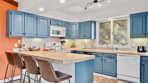 A modern kitchen with blue cabinets, a central island with bar stools, a microwave, and a dishwasher. - Divine Destiny Vacation Home at Windcliff (Estes Park)
