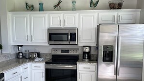 A modern kitchen with white cabinets, stainless steel appliances, and decorative butterfly wall art. - Pelican Sound Golf and River Club (Estero)