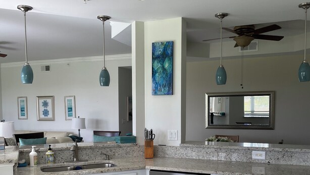 A modern kitchen with white cabinets, a stainless steel dishwasher, and blue pendant lights. - Pelican Sound Golf and River Club (Estero)