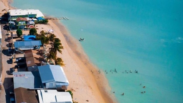 An aerial view of a coastal area with a beach, several buildings, and boats. - The Good Vibes House (Cabo Rojo)