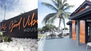 A hotel sign with the text "The Good Vibes" and a modern building with a palm tree and outdoor seating area.