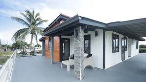 A modern house with a covered patio, stone pillars, and a view of palm trees. - The Good Vibes House (Cabo Rojo)