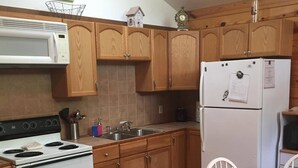 A kitchen with wooden cabinets, a white stove, a refrigerator, and a dining table with chairs. - Rio Cancion on Guadalupe Cabin 2 (New Braunfels)