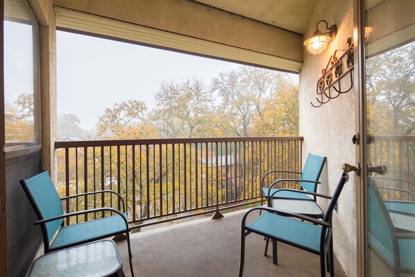 A balcony with two chairs and a table, overlooking a view of trees with autumn foliage.