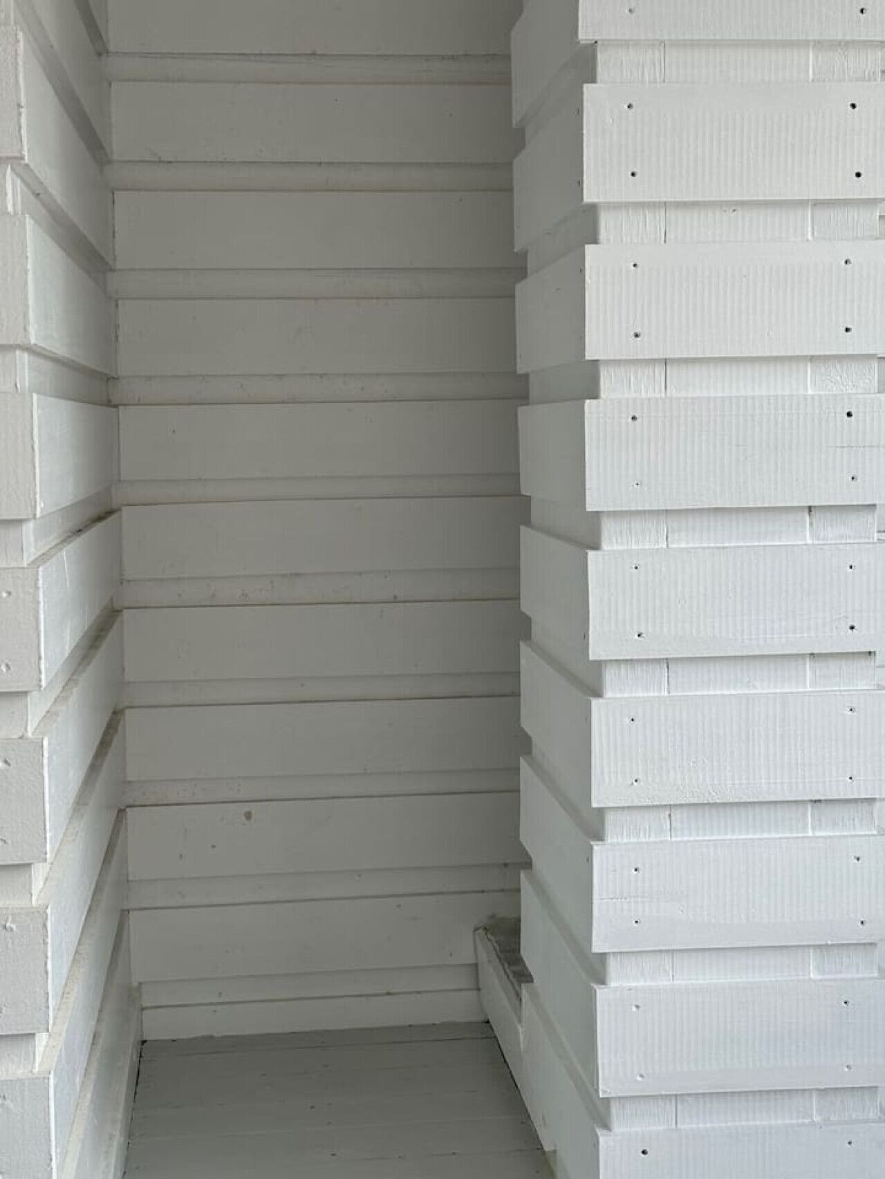 A corner of a room with white wooden paneling and a small window.