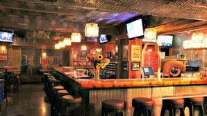 Una zona de bar con taburetes, una barra y televisores instalados en la pared.