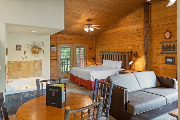 A wooden cabin with a bed, a sofa, a dining table, and a bathtub.