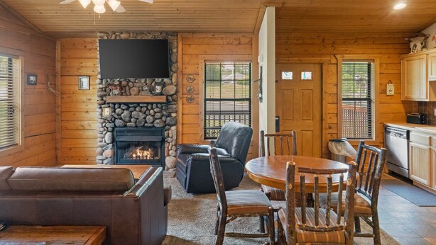 A cozy cabin interior with a stone fireplace, leather seating, a dining area, and a kitchen. - Rustic Studio Cabin with King Bed and Jacuzzi Tub (Branson)