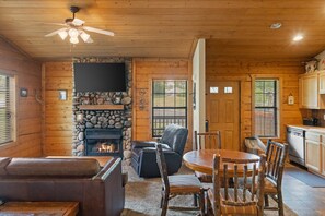 A cozy cabin interior with a stone fireplace, leather seating, a dining area, and a kitchen.