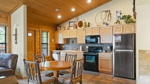 A kitchen with wooden cabinets, a stainless steel refrigerator, and a dining area with a wooden table and chairs. - Rustic Studio Cabin with King Bed and Jacuzzi Tub (Branson)