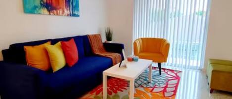 Una sala de estar con un sofá azul, cojines coloridos, una mesa de centro blanca y una alfombra vibrante.