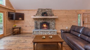 Un salon chaleureux avec une cheminée en pierre, des murs en bois, un canapé en cuir et un téléviseur à écran plat.