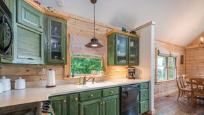 Une cuisine rustique avec des meubles en bois, un lave-vaisselle encastré et une fenêtre donnant sur un espace verdoyant.