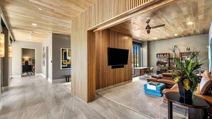 Un vaste espace de vie doté d’un plafond en bois, d’un téléviseur à écran plat, d’une bibliothèque et d’un coin salon confortable.