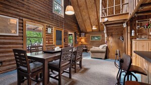 A log cabin interior with a dining area, a sofa, and a loft space. - LuckyStryk - Classic Barker Loop Camp on Mooselookmeguntic (Oquossoc)