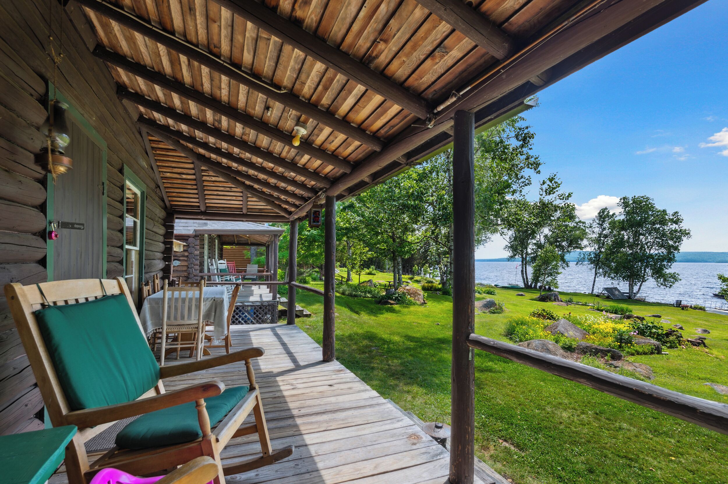 A wooden deck with rocking chairs, a table, and a view of a lake.