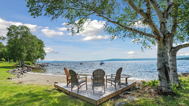 A wooden deck with Adirondack chairs overlooking a lake, surrounded by trees and a grassy area. - LuckyStryk - Classic Barker Loop Camp on Mooselookmeguntic (Oquossoc)