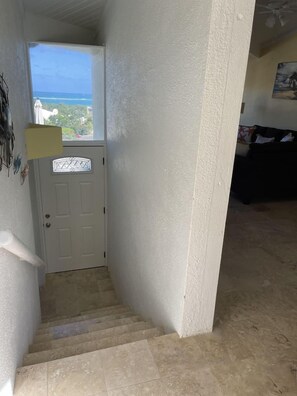 A hallway with a white door, a small window, and a staircase leading to an upper floor.