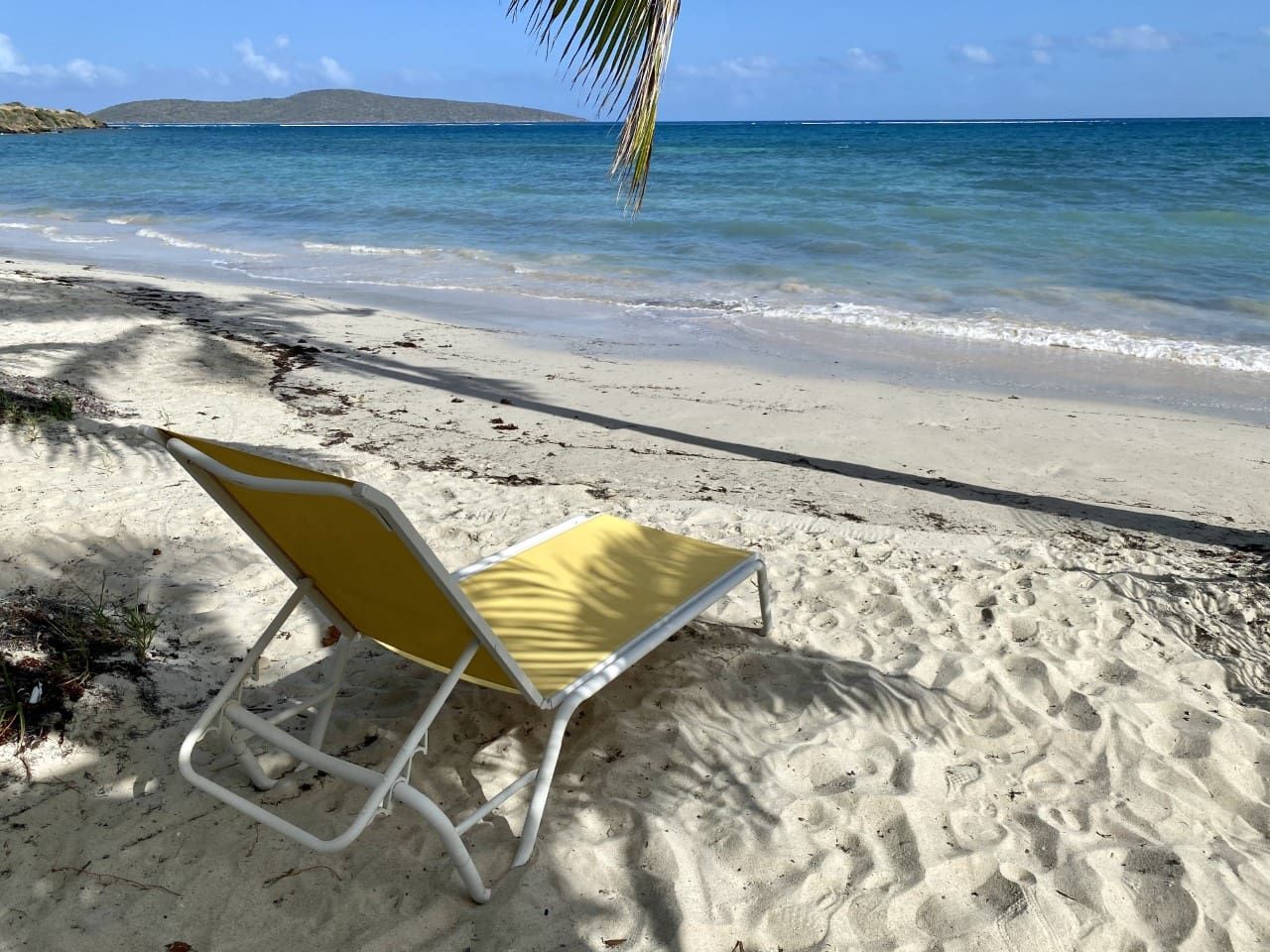 Una playa con una sola silla de playa amarilla y blanca.