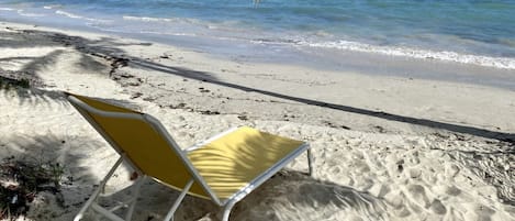 Una playa con una sola silla de playa amarilla y blanca.