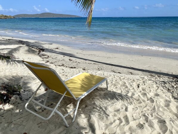 A beach with a single yellow and white beach chair.