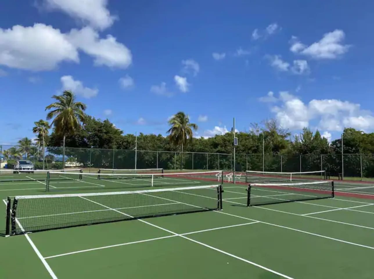 A tennis court with multiple courts, a net, and a fence.